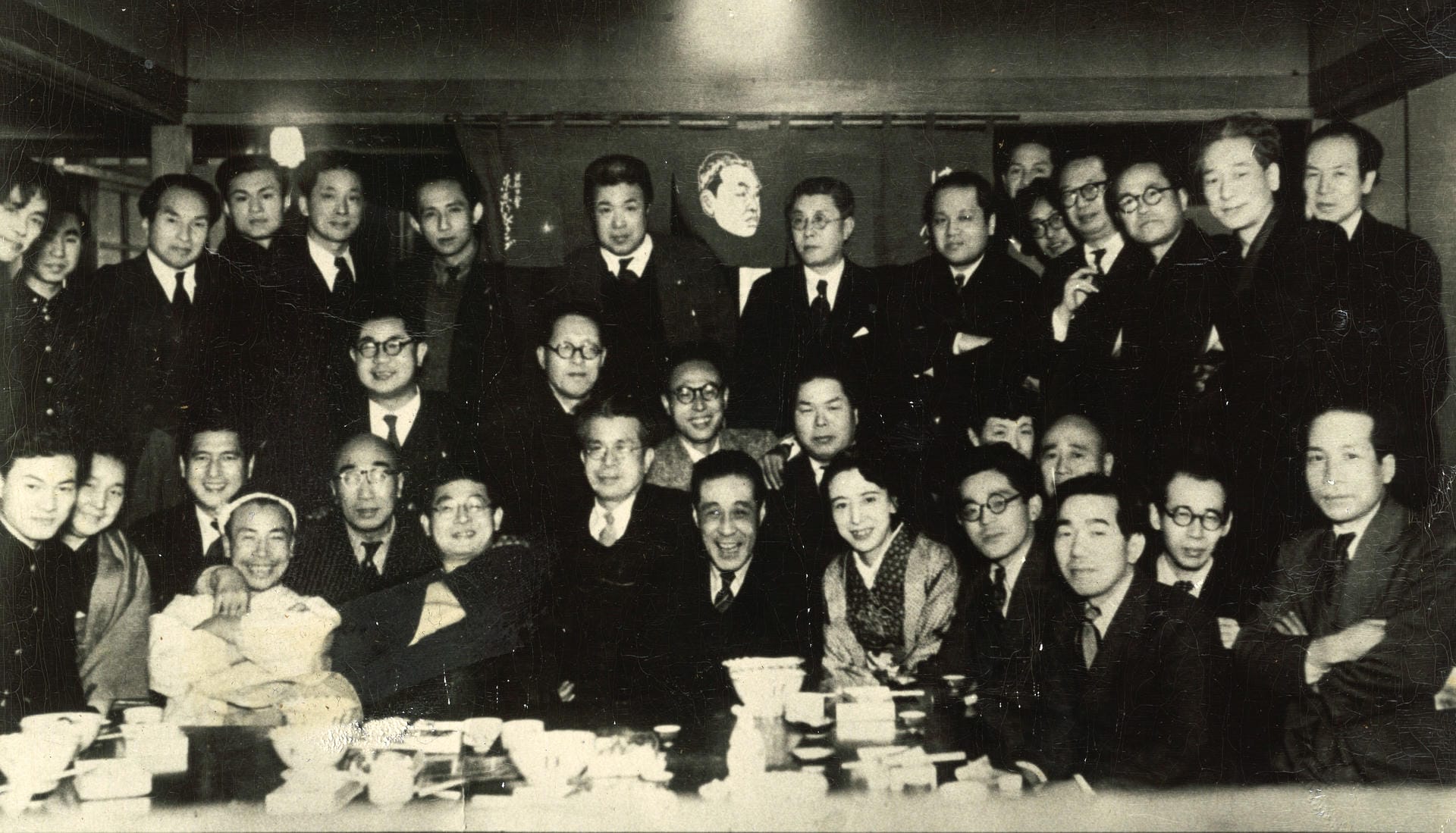 廿七会の集合写真。はちまき姿の店主・寅吉の右隣、寅吉の肩に手を置いているのが江戸川乱歩先生。その右で腕を組むのが海音寺潮五郎先生。寅吉の左後ろは、昭和の大俳優・佐野周二さん。